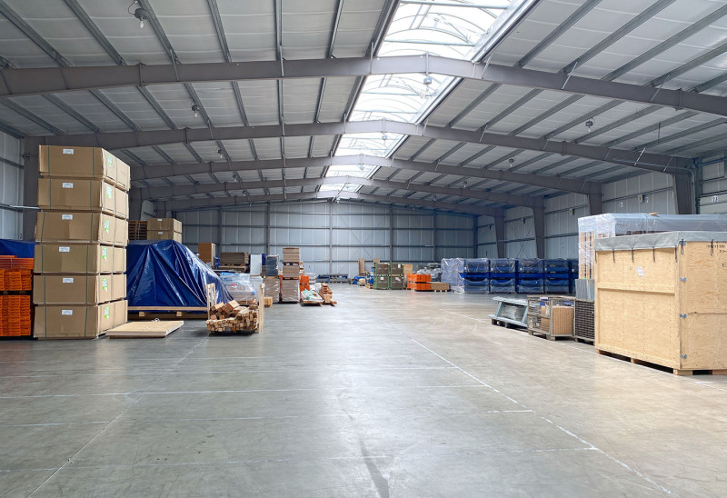 You look into the depth of a newly built warehouse. Inside it, on both sides, there are many packed goods.