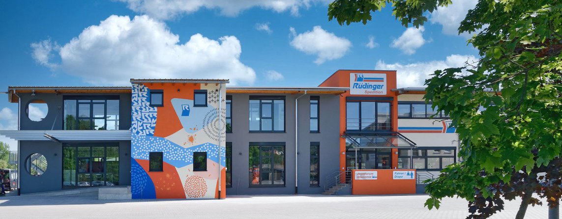 On a huge meadow, a rabbit is sitting on the left and a fox on the right and seem to be talking. In the background you can see buildings and trucks of the forwarding agency.