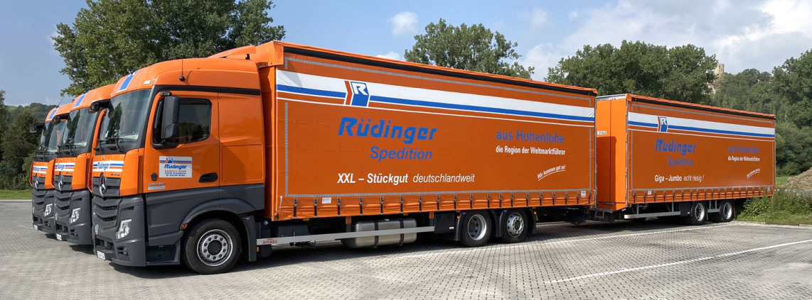 Three tarpaulin low-loaders are standing next to each other. The viewer looks diagonally to the side of the vehicle in front. Closest to the viewer is a mega liner, which in Germany is a Lang-Lkw with a trailer.