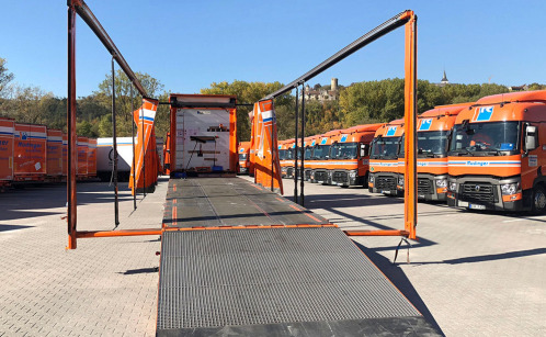Between two rows of trucks stands a tarpaulin low loader, which you look at from the back. All tarpaulins are open, so that only the skeleton, the linkage is left. At the back, you can drive up on a full back wall.