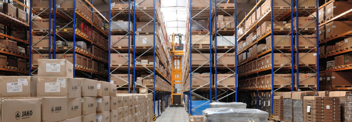 You can see into several narrow aisles of a warehouse. All of them are full of goods. In the middle is a narrow aisle forklift in orange color. The driver sits about 5 meters above the ground.