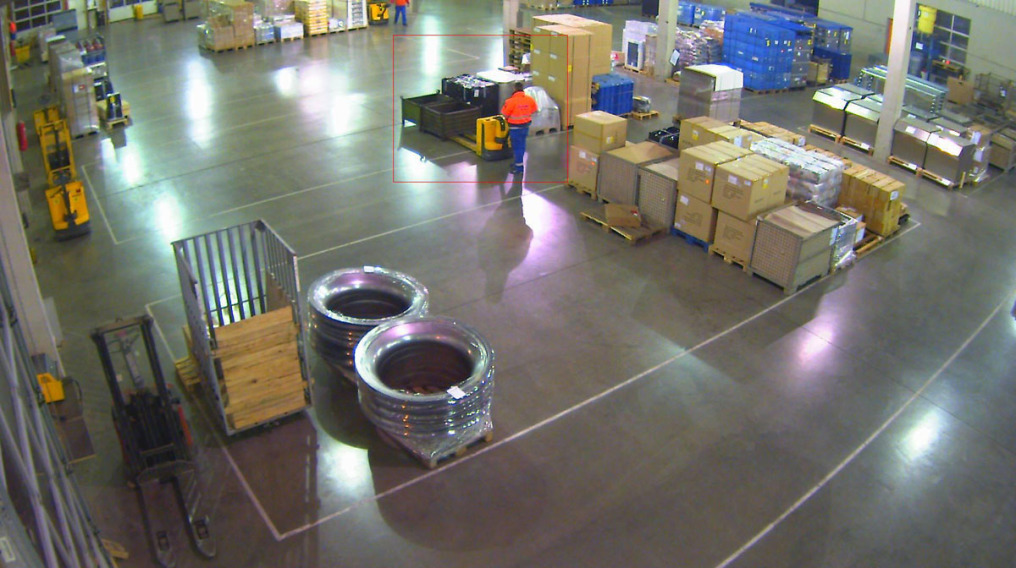The transshipment hall from the perspective of the DIVIS surveillance camera. You can see various packed goods and an employee who wants to pick up goods with a lift truck.