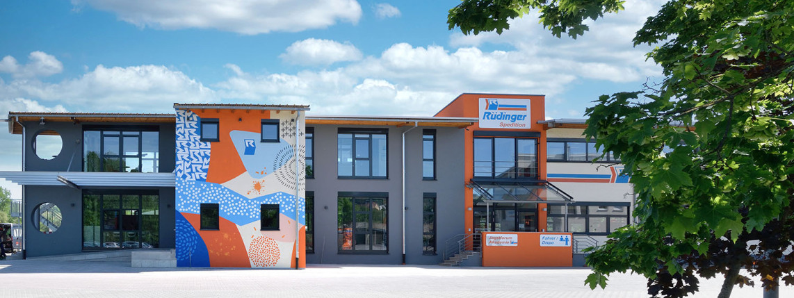 Three cubes at administrative building, left, are new and form the "Jagstforum". The right and left are gray, the one in the middle is a facade artwork in orange and blue. In the right third you can see the last phase of construction.