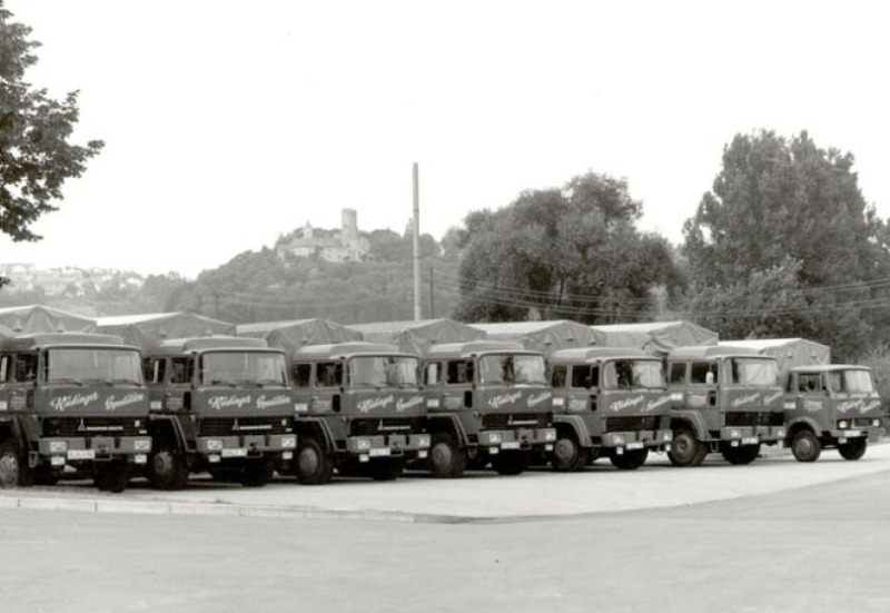 There are six ancient trucks on a historical black and white photo. In the background you can see trees, forest and the castle in Krautheim.