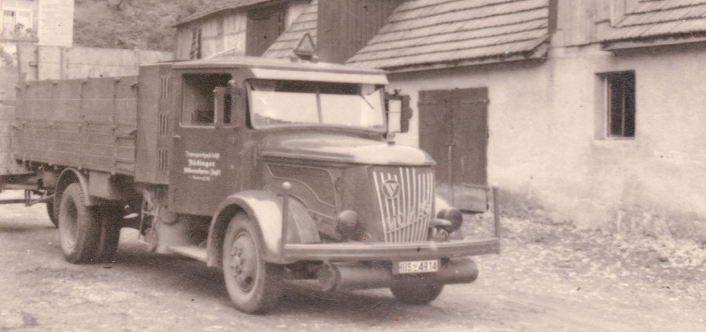 You look at a historic Magirus-Deutz truck from the side and front. It is standing in front of an agricultural building. It's an almost 90-year-old photo in black and white.