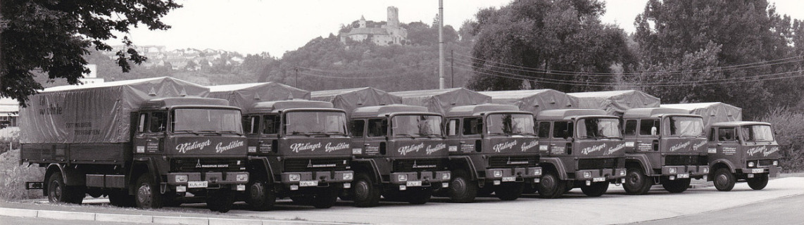It is an ancient historical photo in black and white. Seven trucks, already at that time with tarpaulin, are neatly lined up. In the background you can see Krautheim Castle.
