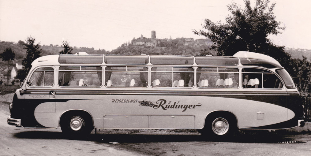 On a black and white photo you can see a touring bus completely from the side with driving direction to the left. In the background is the castle Krautheim. On the bus is written "Reisedienst Rüdinger".